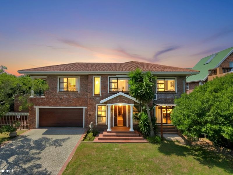 A well-maintained double-story brick house featuring a tiled roof, paved driveway, double garage, and an inviting covered entrance porch set within a landscaped garden.