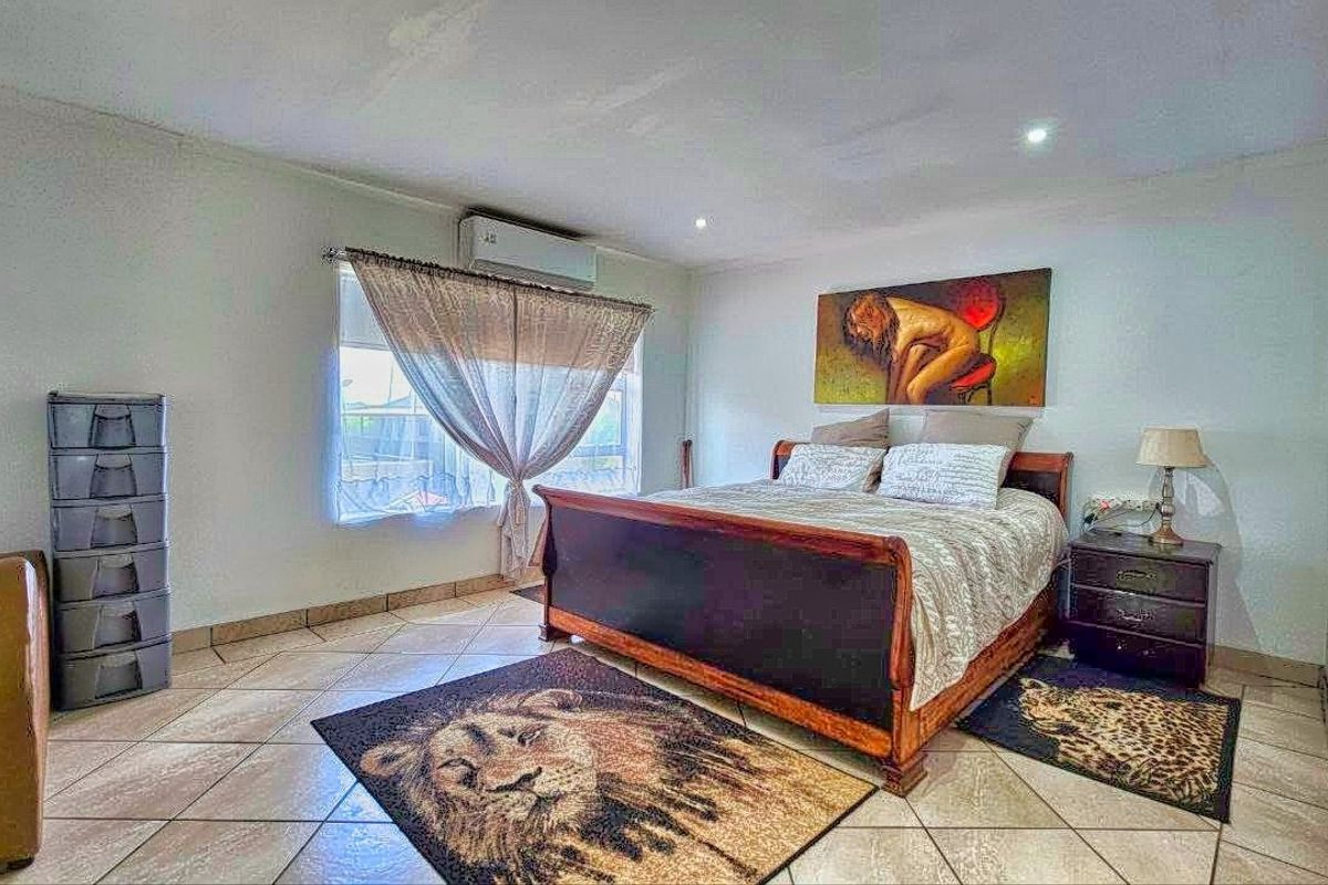 A spacious bedroom featuring tiled flooring, recessed downlighting, and a wall-mounted split-system air conditioning unit.