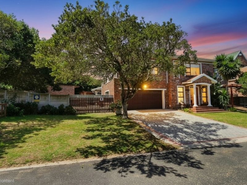 A well-maintained double-story brick house featuring a paved driveway, double garage, and a covered entrance porch set within a landscaped front garden.