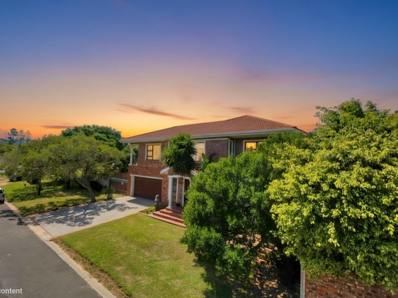 A well-maintained double-story brick house featuring a tiled roof, paved driveway, and an integrated double garage, set within a landscaped residential street.