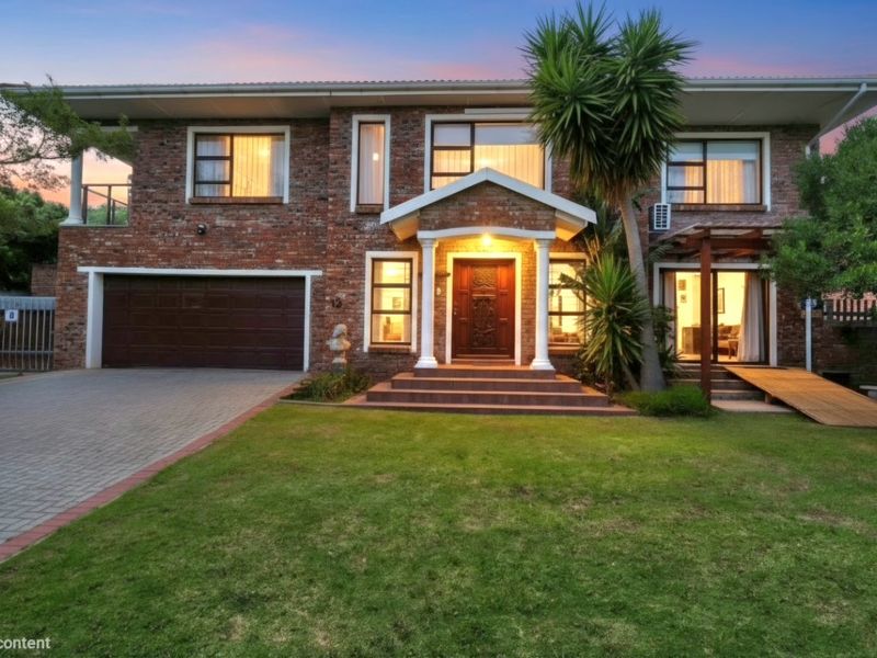 A well-maintained double-story brick residence featuring a paved driveway, double garage, and an inviting covered entrance with classic columns and a landscaped front lawn.