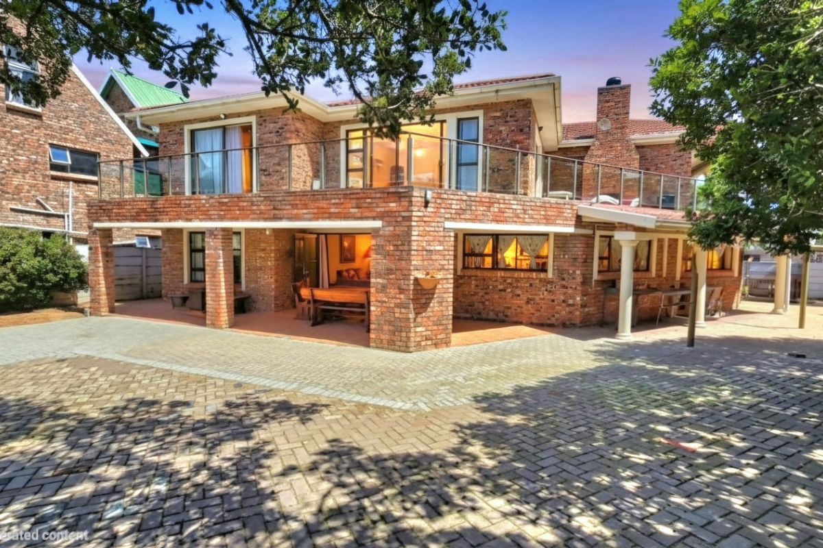 A spacious double-story brick home featuring a large paved courtyard, covered patio area, and an expansive upper-level balcony with glass balustrades.