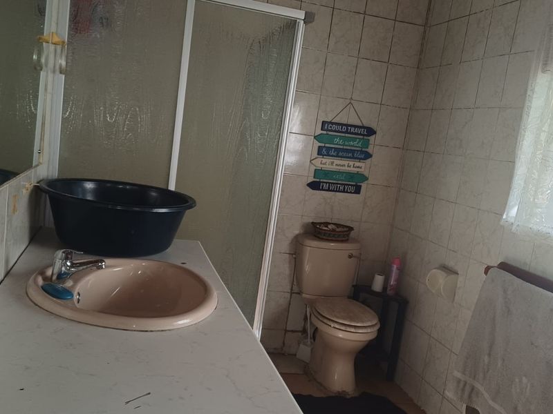 A dated bathroom featuring a vanity basin, shower enclosure, and toilet with full wall tiling, requiring cosmetic updates to improve its overall condition.