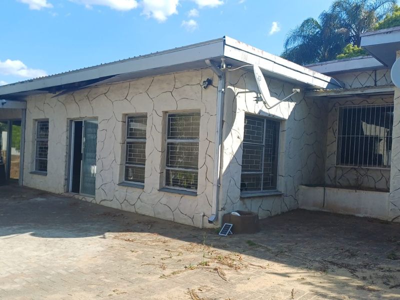 Rear exterior view of the house featuring a stone-clad facade, security bars on windows, and a paved patio area.