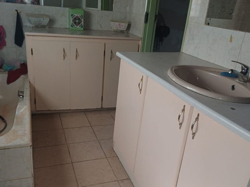 A dated bathroom featuring built-in vanity cabinets, a tiled bathtub, and ceramic flooring, offering significant potential for a modern renovation.