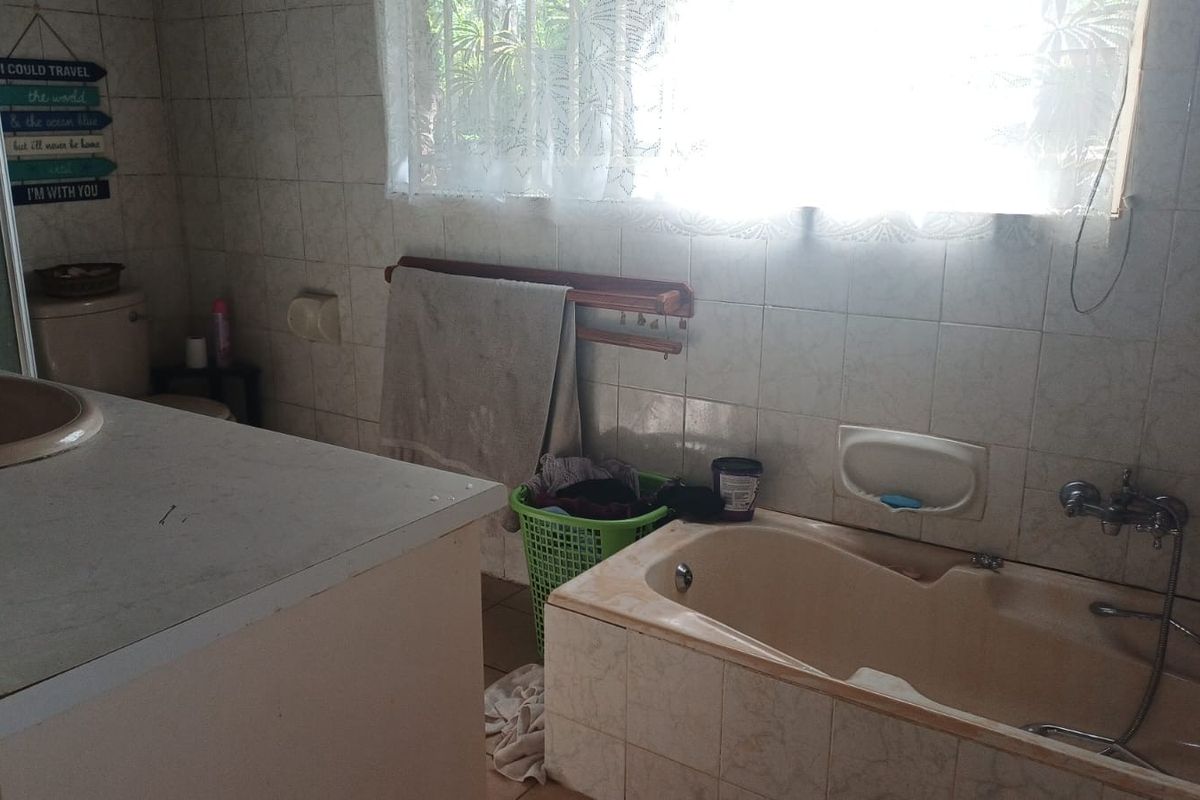 A dated bathroom featuring a built-in bathtub, vanity basin, and tiled wall finishes, offering potential for a modern renovation.