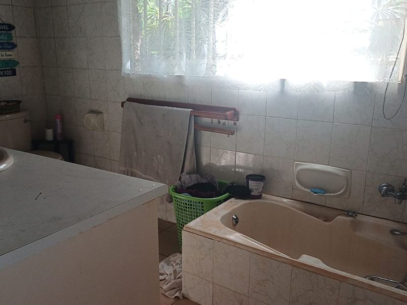 A dated bathroom featuring a built-in bathtub, vanity basin, and tiled wall finishes, offering potential for a modern renovation.