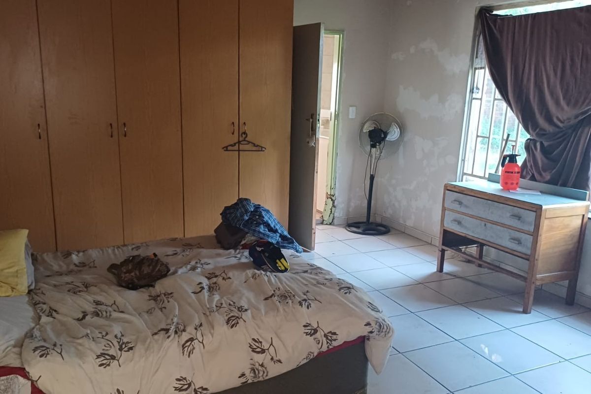 A bedroom featuring built-in cupboards and tiled flooring, currently requiring cosmetic attention to the walls and door frame.
