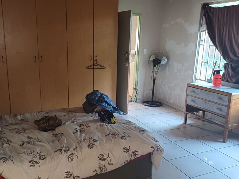 A bedroom featuring built-in cupboards and tiled flooring, currently requiring cosmetic attention to the walls and door frame.