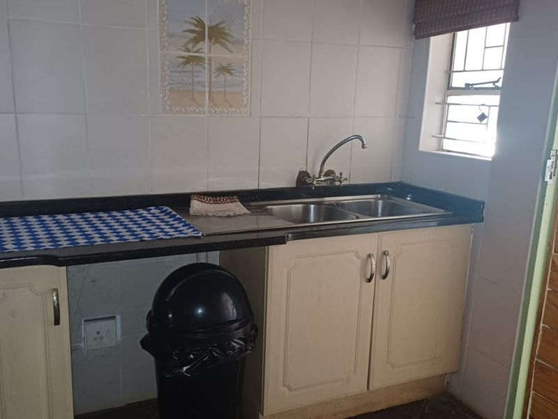 A functional scullery area featuring a double bowl sink, laminate cabinetry, and tiled backsplash, providing a practical space for food preparation and cleanup.