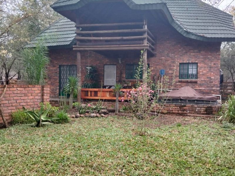 Rear view of a double-story brick house featuring a wooden balcony, tiled roof, and a landscaped garden area.