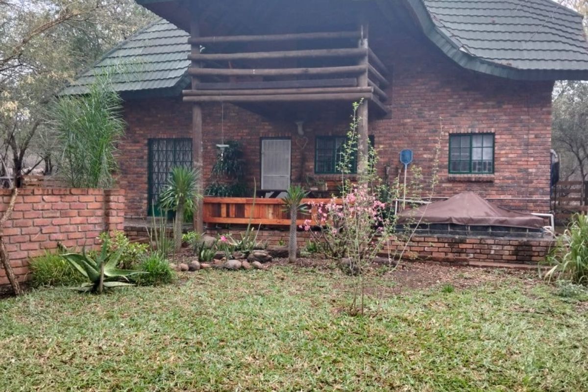 Rear view of a double-story brick house featuring a wooden balcony, tiled roof, and a landscaped garden area.