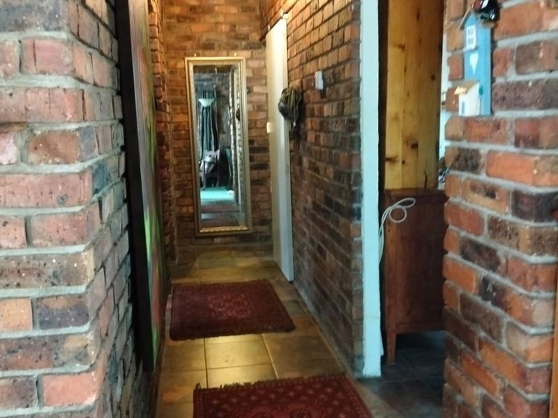 A rustic hallway featuring exposed brick walls, tiled flooring, and an exposed timber beam ceiling, creating a warm and textured transition space.