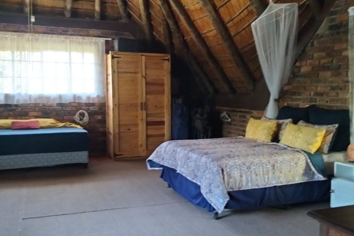 Spacious bedroom featuring a unique vaulted thatched roof with exposed timber rafters and rustic exposed brick walls, offering a distinctive architectural character.