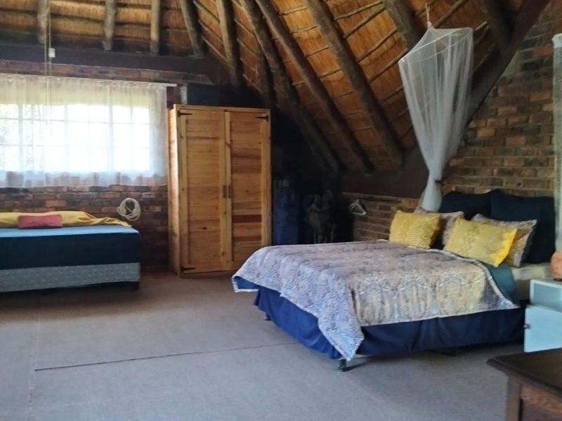 Spacious bedroom featuring a unique vaulted thatched roof with exposed timber rafters and rustic exposed brick walls, offering a distinctive architectural character.