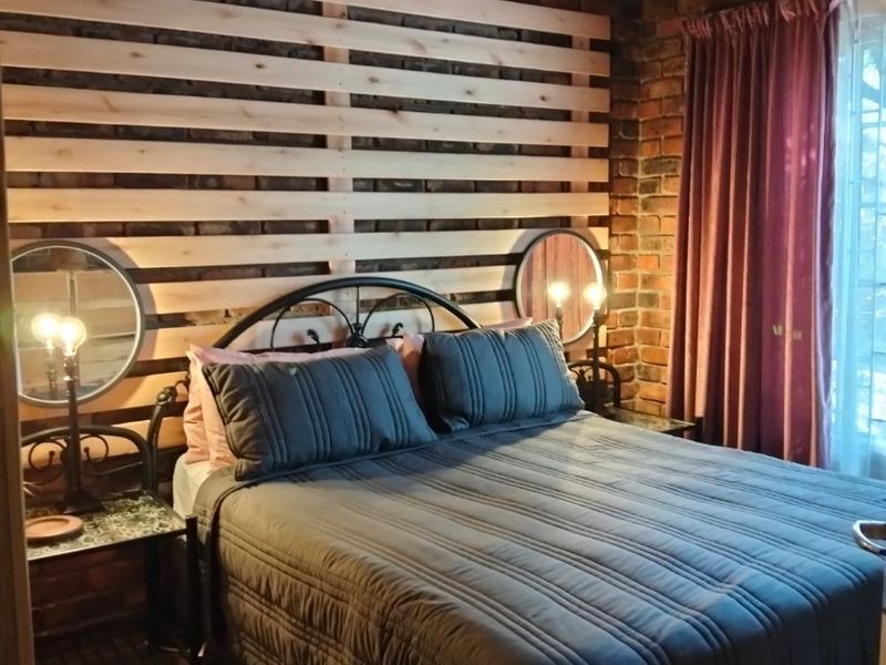 A cozy bedroom featuring exposed brick walls, timber ceiling beams, and a decorative timber slat feature wall with tiled flooring.