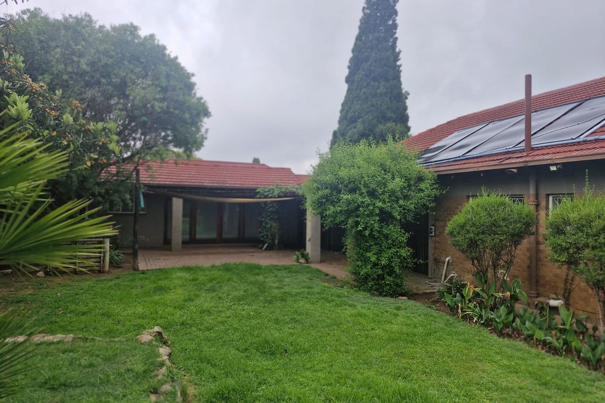 A rear garden view featuring a lawn, paved patio area, and a brick house exterior equipped with solar water heating panels on the roof.