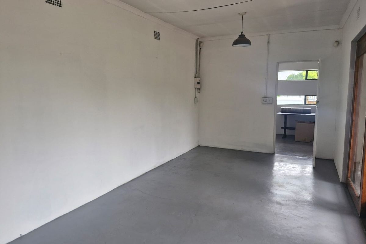 An empty, neutral-toned living space featuring painted concrete flooring, pendant lighting, and exposed electrical conduit, offering a blank canvas for renovation.