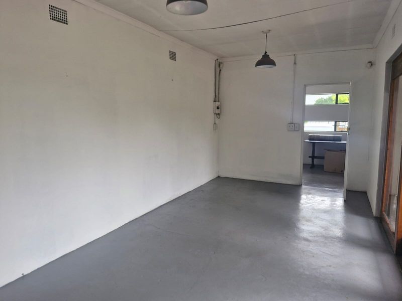 An empty, neutral-toned living space featuring painted concrete flooring, pendant lighting, and exposed electrical conduit, offering a blank canvas for renovation.