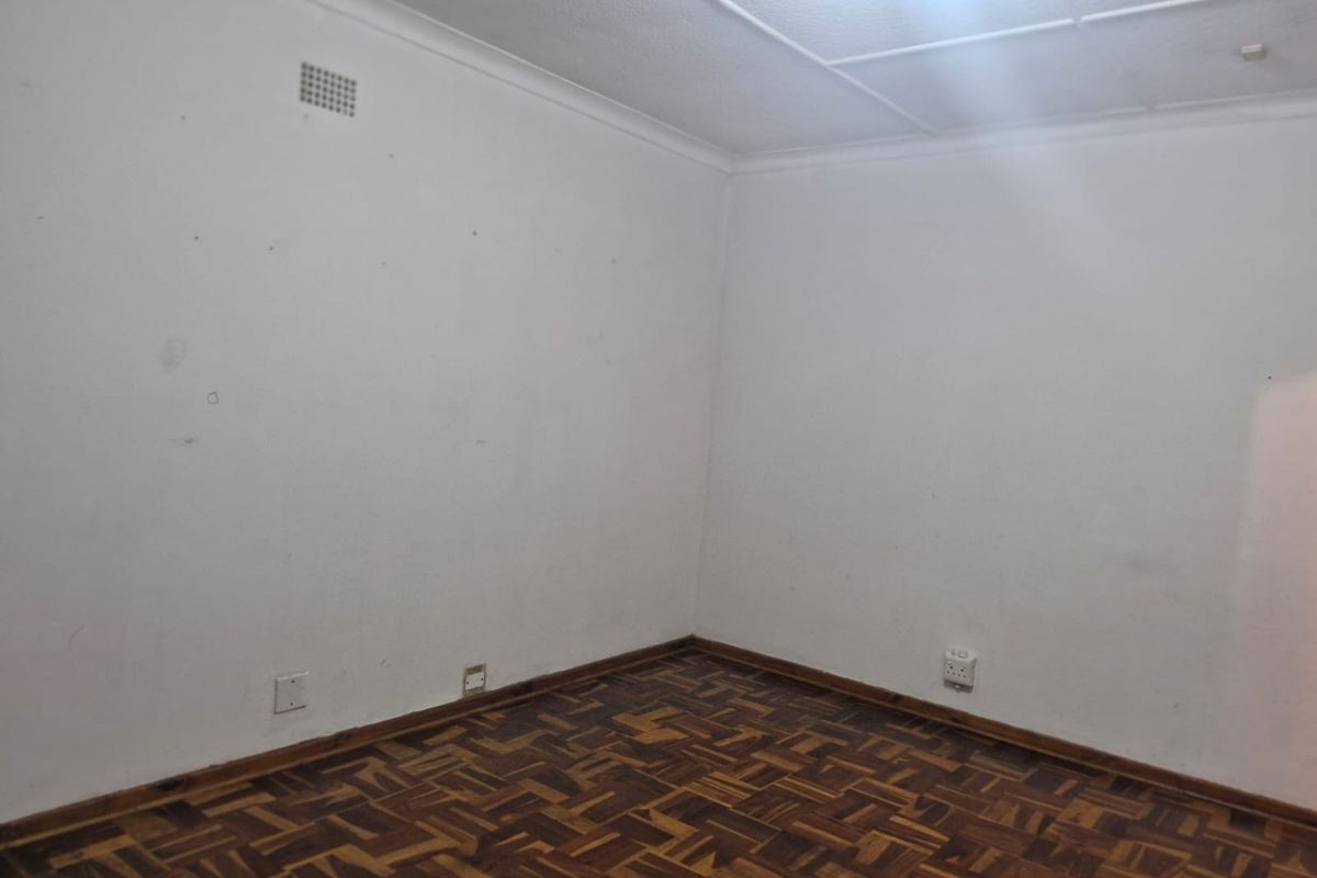 An empty bedroom featuring traditional parquet flooring, ceiling tiles, and plain white walls, offering a blank canvas for renovation or interior design.