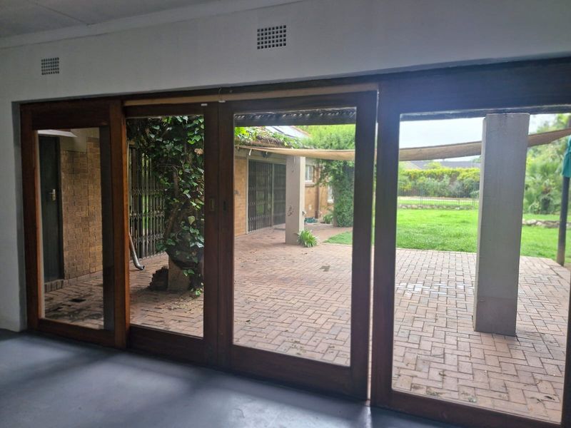 An interior view looking out through large wooden sliding doors onto a brick-paved patio and garden area.