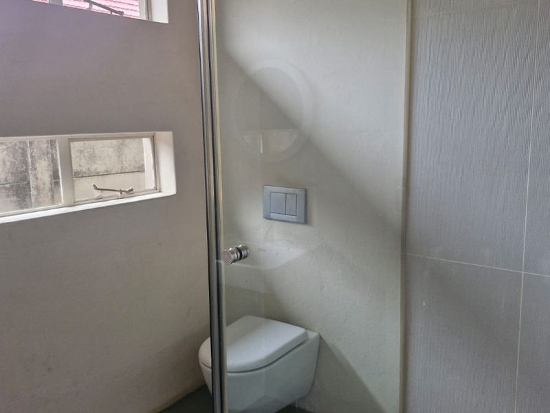 A modern bathroom featuring a wall-mounted toilet with a concealed cistern, a glass-enclosed shower, and neutral wall tiling.