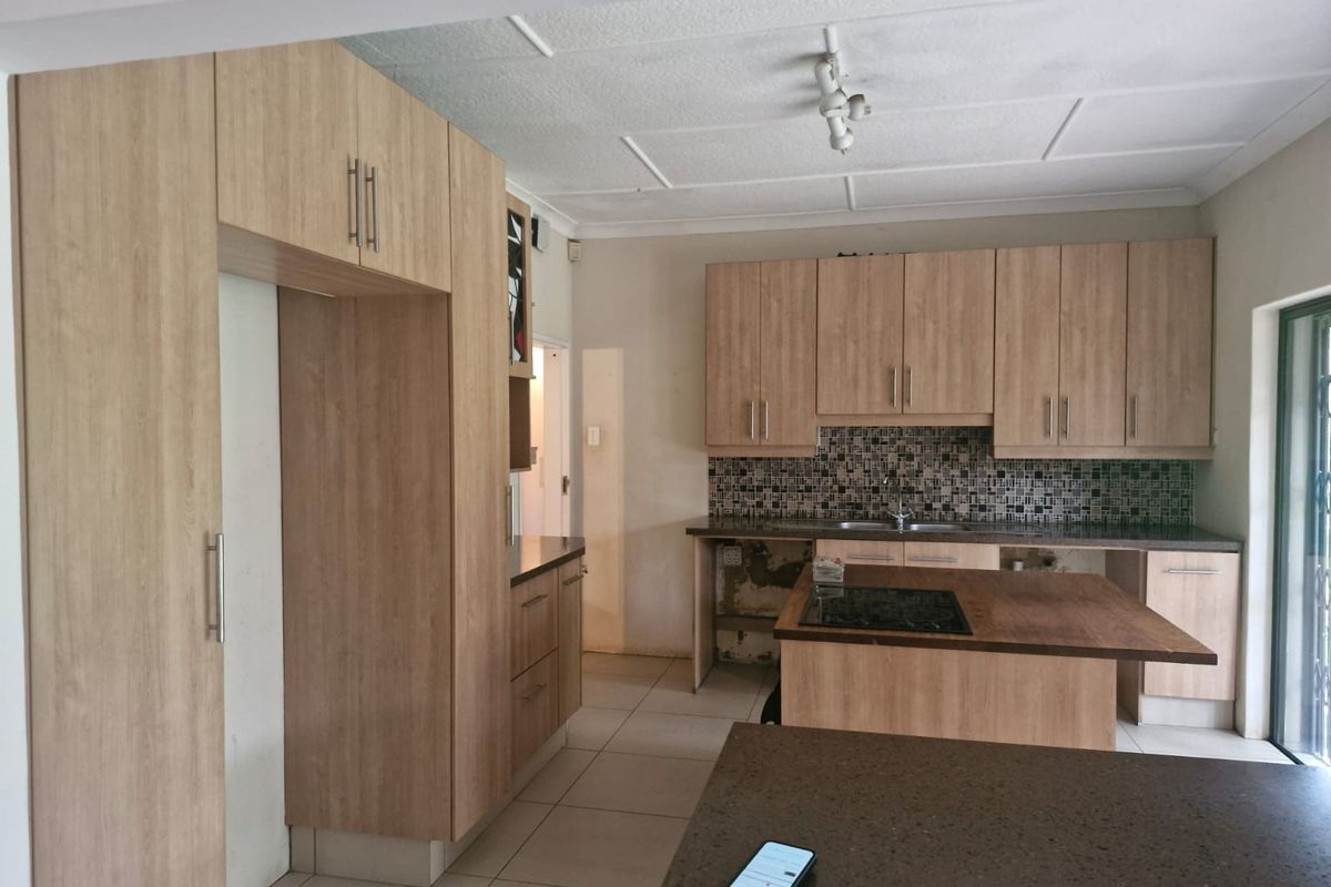 Kitchen featuring light wood-look cabinetry, a central island with a hob, mosaic tile backsplash, and tiled flooring. Requires minor repairs to cabinetry and wall finishes.