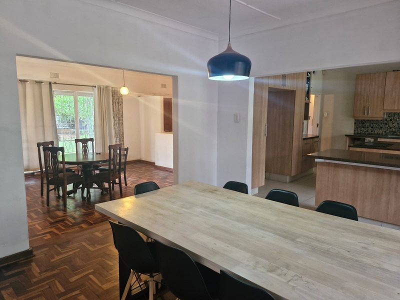 Spacious open-plan living and dining area featuring classic parquet flooring, flowing into a functional kitchen with modern cabinetry and stone countertops.