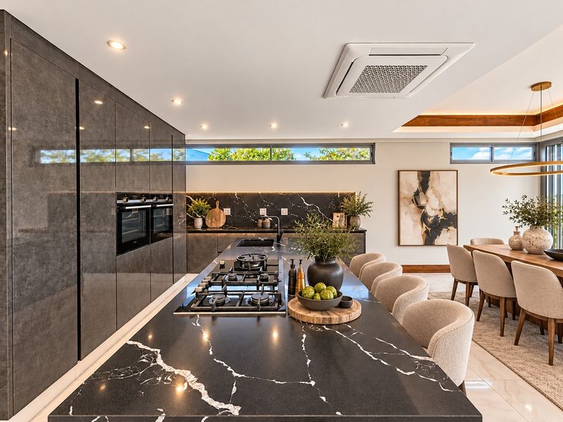 Modern open-plan kitchen featuring a large marble island with integrated gas hob, high-end cabinetry, double ovens, and sleek marble backsplash with recessed lighting.