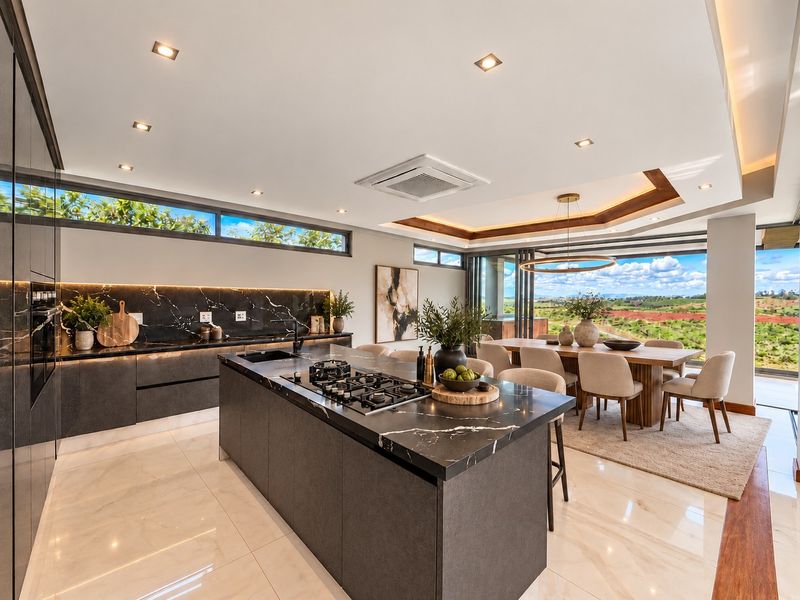 Modern open-plan kitchen and dining area featuring a large island with gas cooktop, premium stone finishes, and expansive views through sliding glass doors.