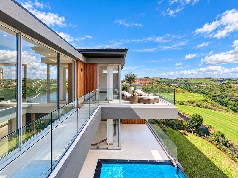Modern elevated balcony featuring glass balustrades, tiled flooring, and seamless access to the interior, overlooking a swimming pool and expansive golf course views.