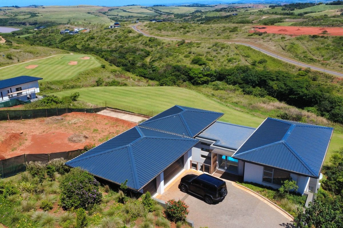 Aerial view of a modern house with a metal roof, paved driveway, and garage, situated in a scenic estate setting.