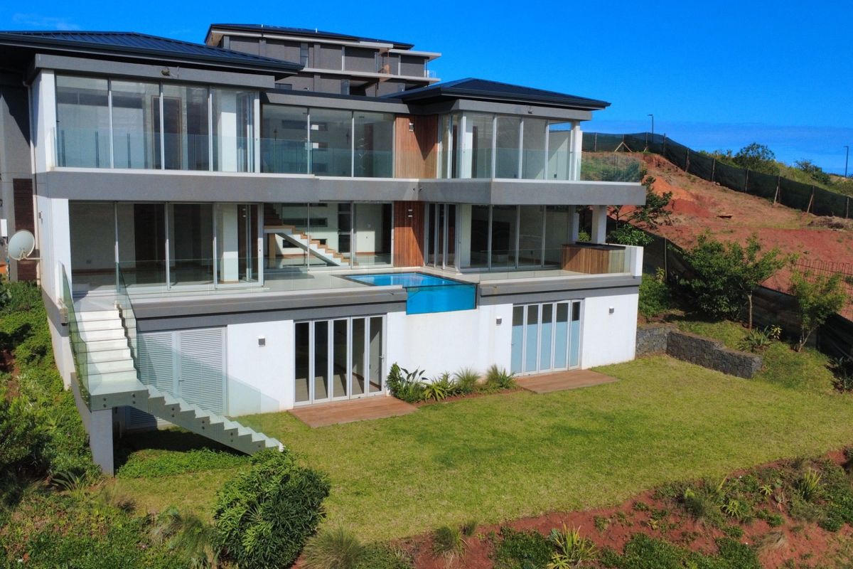 Modern multi-level residence featuring a rear swimming pool, extensive glass facades, timber decking, and landscaped garden areas.