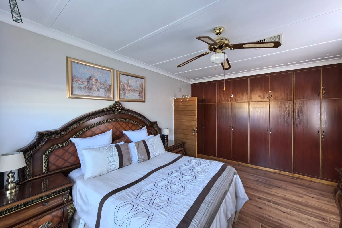 Spacious bedroom featuring extensive dark wood built-in cupboards, a ceiling fan, and laminate flooring.