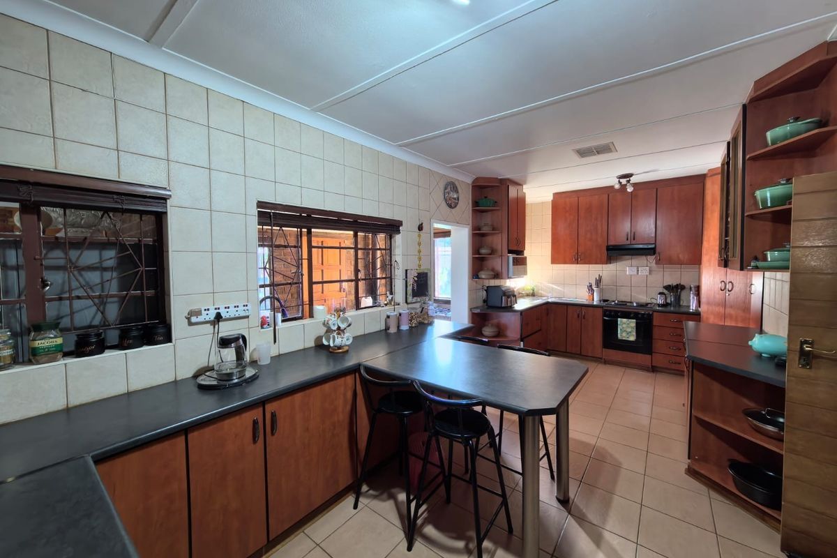 A spacious kitchen featuring extensive wooden cabinetry, dark laminate countertops, a built-in oven with hob, and tiled finishes throughout.