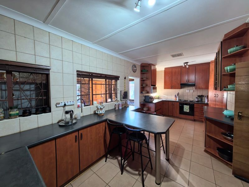 A spacious kitchen featuring extensive wooden cabinetry, dark laminate countertops, a built-in oven with hob, and tiled finishes throughout.