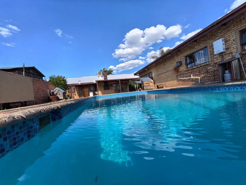 A clear swimming pool set in a backyard area, featuring brick exterior walls and a wall-mounted gas geyser.