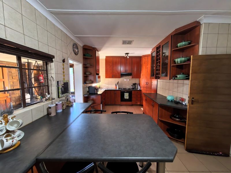 A functional kitchen featuring extensive wooden cabinetry, built-in oven and hob, tiled splashbacks, and a breakfast bar area with tiled flooring.
