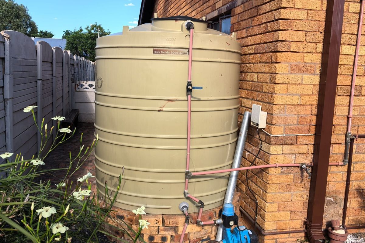 Exterior view of a residential water storage tank and pump system installed against a brick wall.