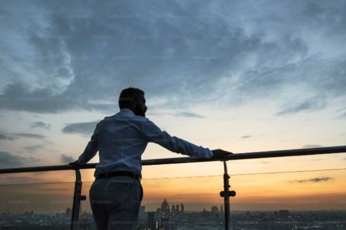 A scenic elevated view of the city skyline at sunset, featuring a modern glass and metal balustrade.