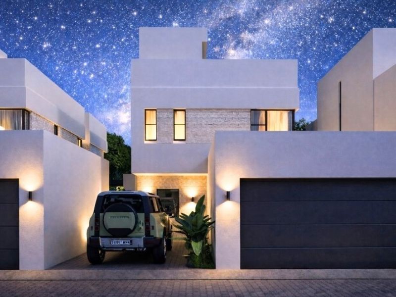 Modern townhouse exterior featuring a double garage, paved driveway, and contemporary architectural design with stone cladding accents and integrated wall lighting.