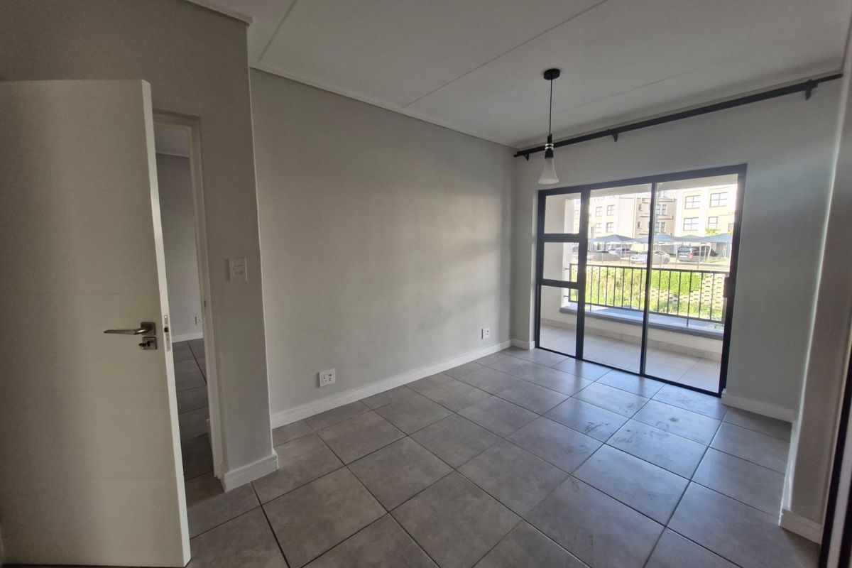 An empty, neutral-toned living room featuring large format floor tiles, a modern pendant light, and a sliding glass door leading to a balcony.