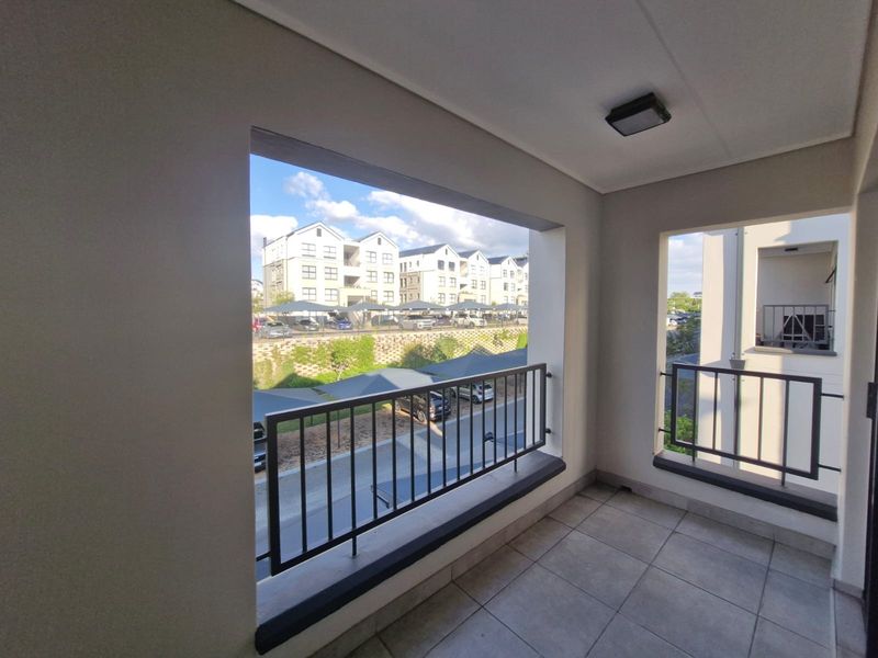 A clean, modern balcony featuring tiled flooring and metal balustrades, offering an open view of the surrounding apartment complex and parking area.