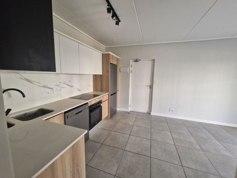 Modern kitchen featuring sleek white and wood-grain cabinetry, stone countertops, integrated appliances, and contemporary tiled flooring in an open-plan layout.