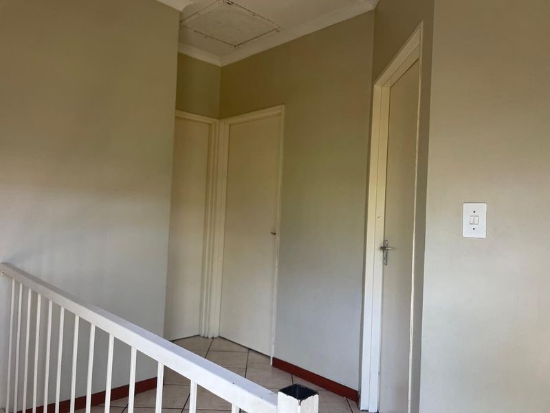A functional hallway area featuring tiled flooring, a metal balustrade, and multiple internal doors providing access to adjacent rooms.