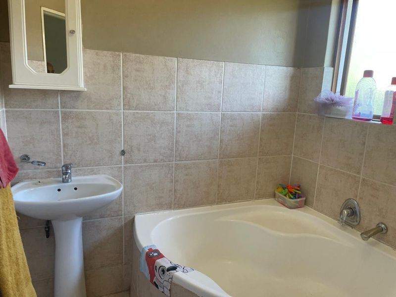 A functional bathroom featuring a pedestal basin, built-in bathtub, and neutral ceramic wall tiling.