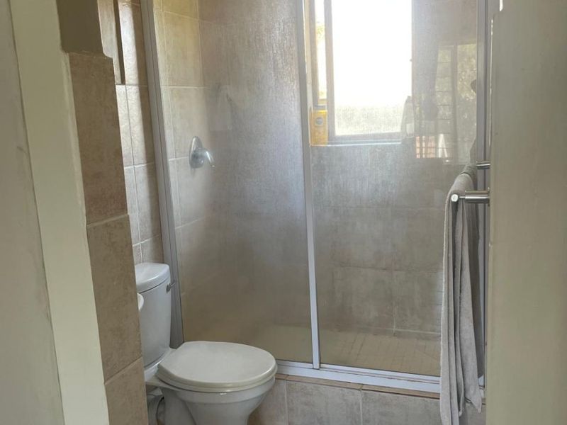 A functional bathroom featuring a tiled shower enclosure, a standard toilet, and neutral wall and floor tiling.