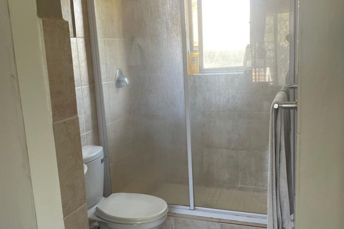 A functional bathroom featuring a tiled shower enclosure, a standard toilet, and neutral wall and floor tiling.