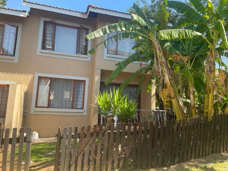 Rear view of a two-story residential property featuring a timber picket fence, patio area, and established garden foliage.