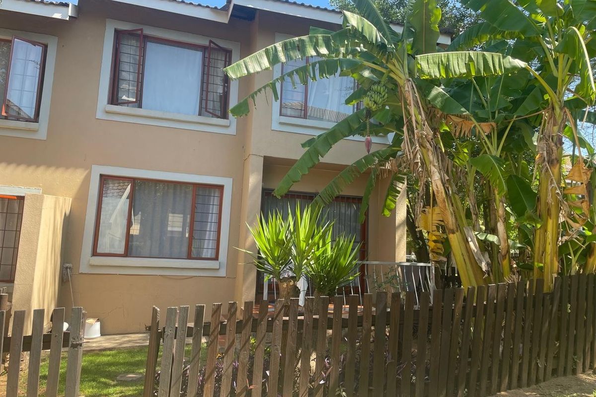 Rear view of a two-story residential property featuring a timber picket fence, patio area, and established garden foliage.